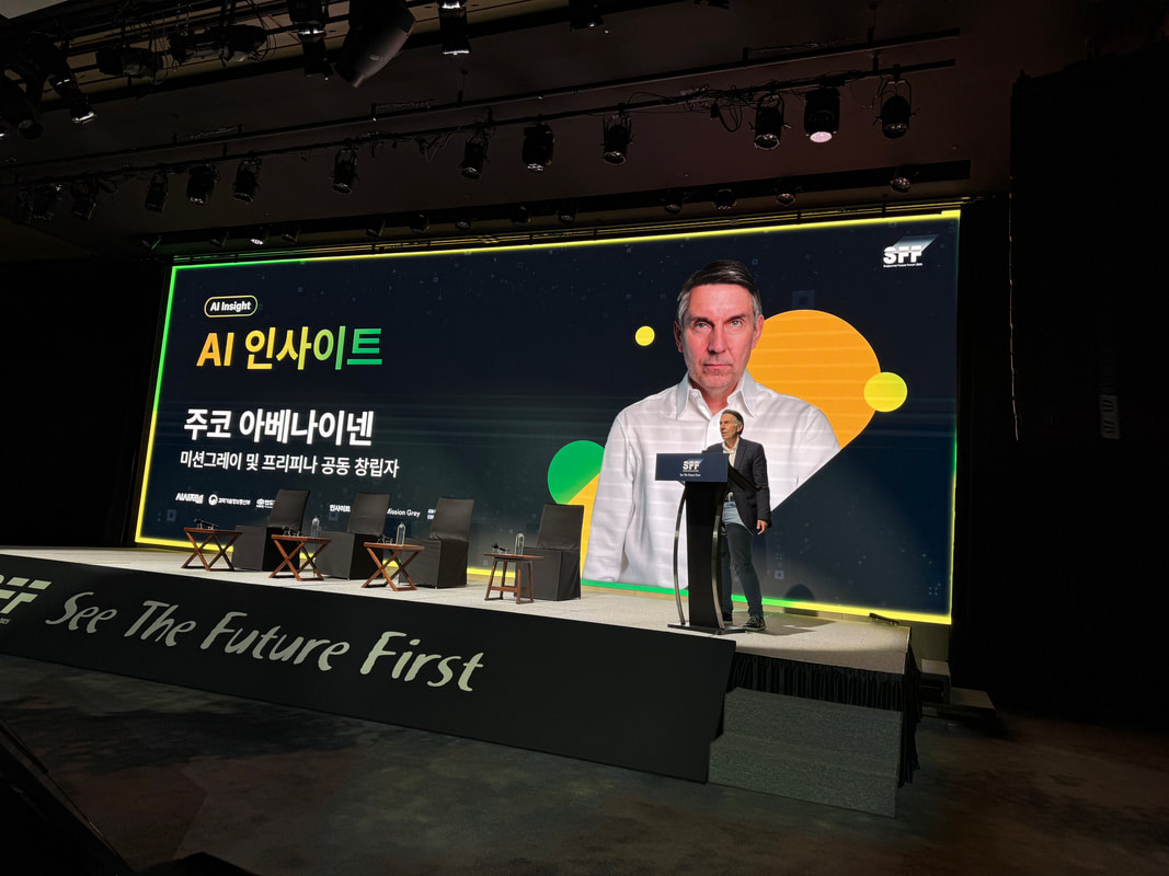 A conference stage in Seoul. The screen behind the lectern introduces Jouko Ahvenainen in Korean as a co-founder of Mission Grey.
